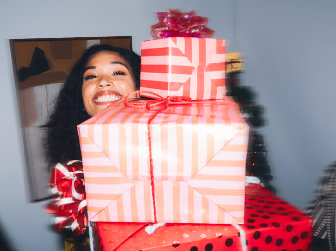 Woman smiling and holding wrapped holiday gifts in front of a Christmas tree