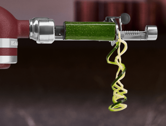 A vegetable spiralizer attachment on an Artisan Plus stand mixer.