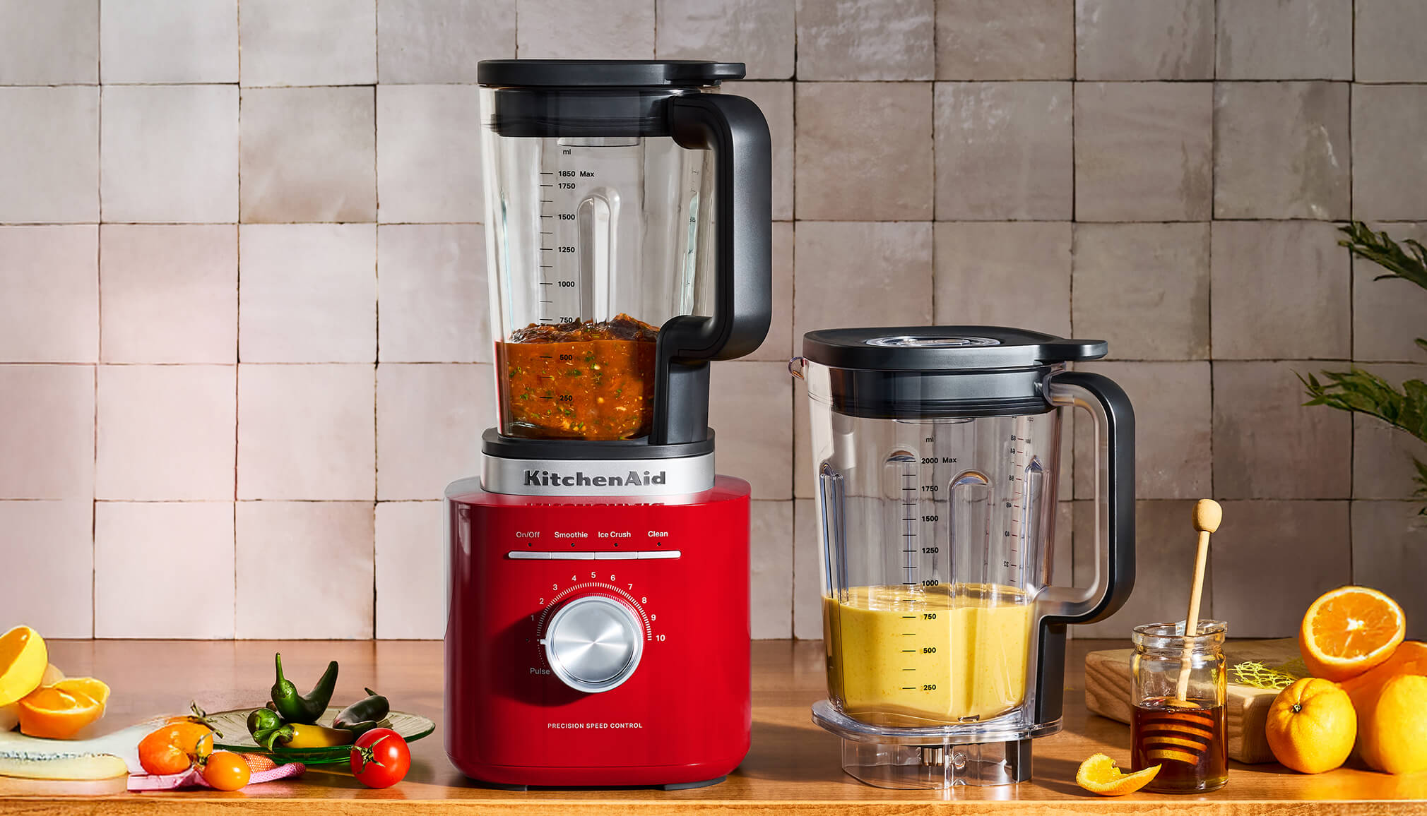 A KitchenAid® blender on a counter with two full jars