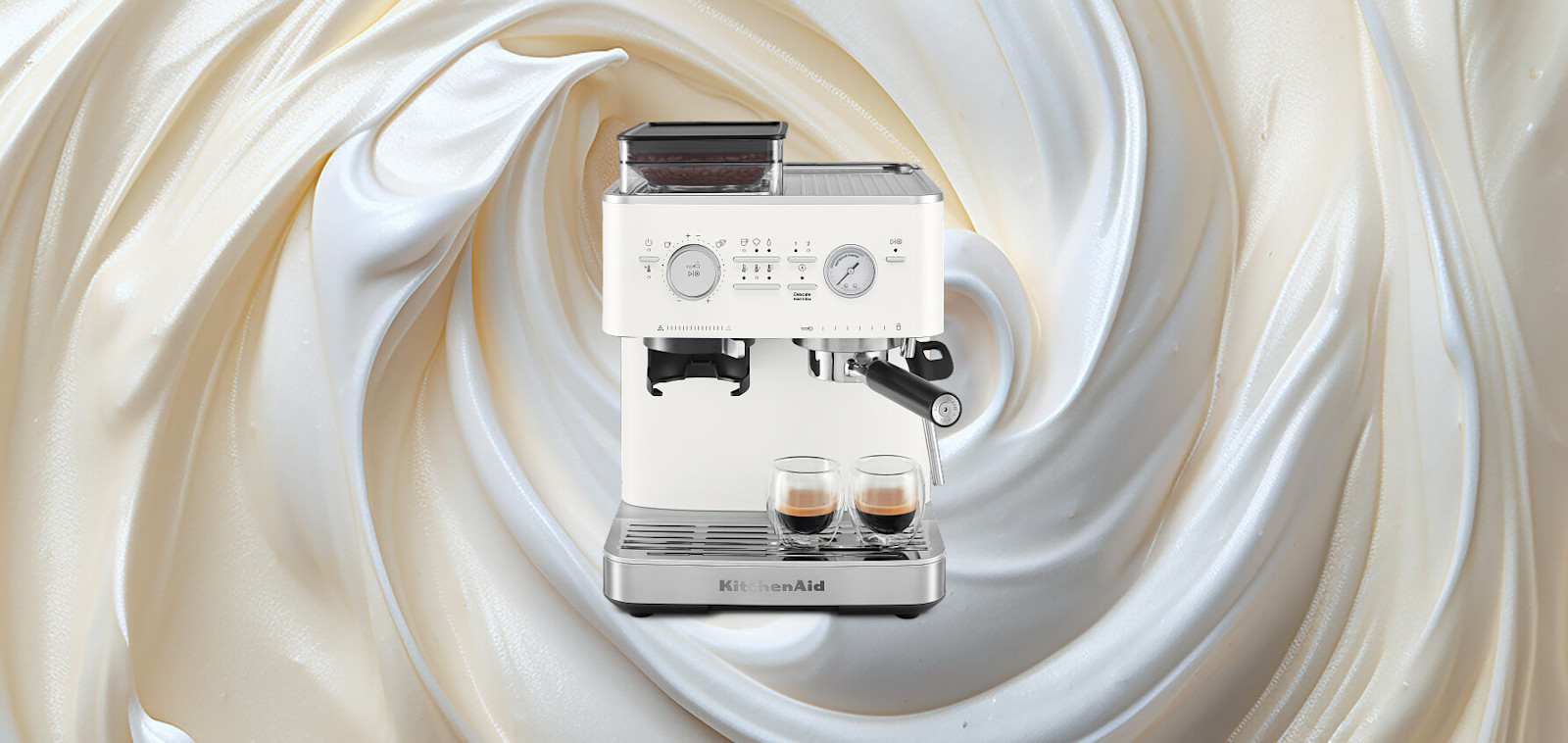 White KitchenAid® semi automatic espresso machine dispensing a latte, set against a swirling cream background