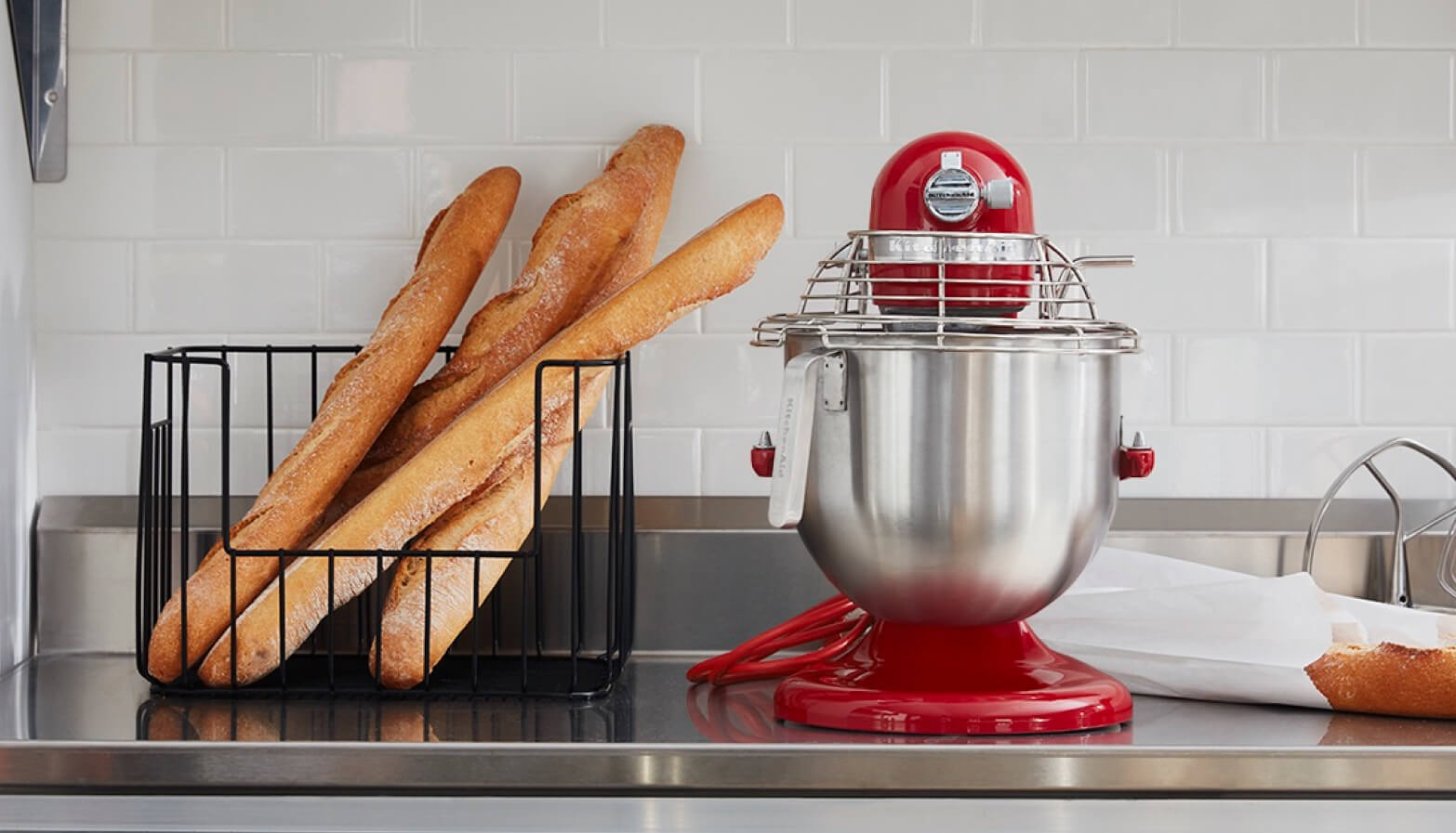 Commercial KitchenAid® stand mixer in Empire Red beside a wire basket of baguettes