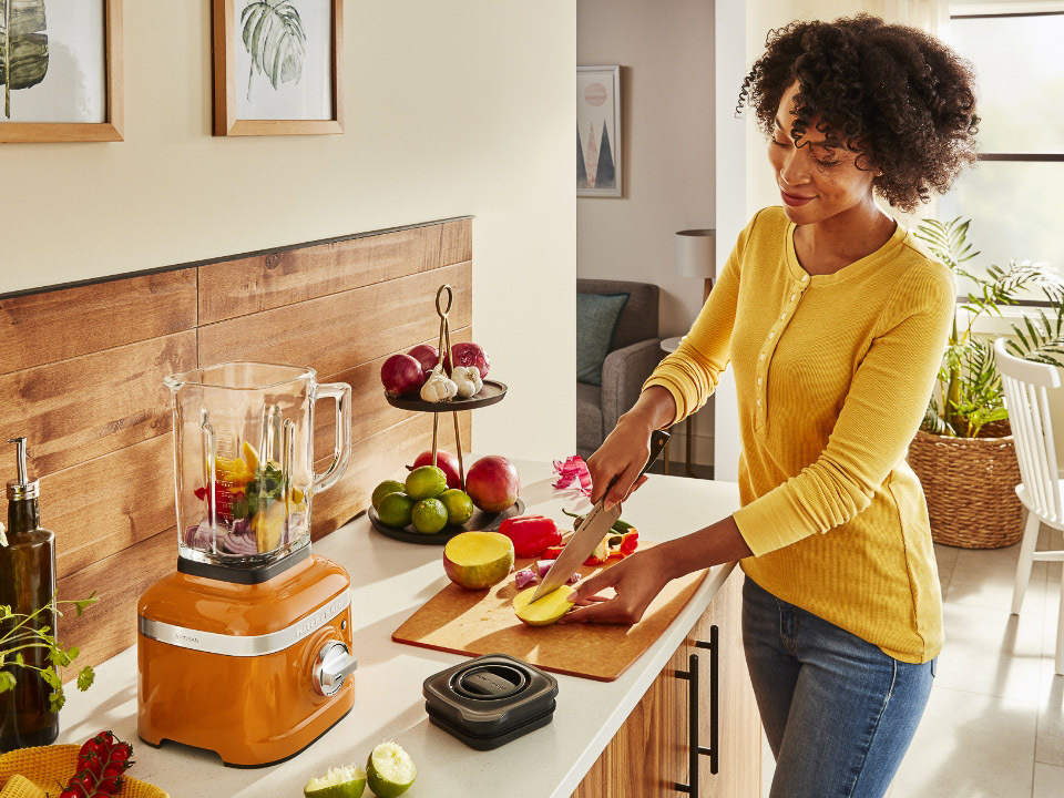 A woman slicing fruit next to a blender