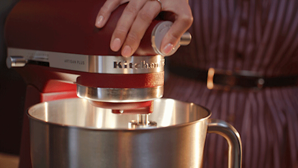 A person lowering the head of their Artisan Plus tilt-head stand mixer.