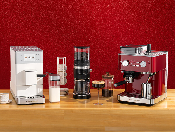 White KitchenAid® espresso machine, coffee grinder, and red espresso machine on a wooden counter with mugs and glassware