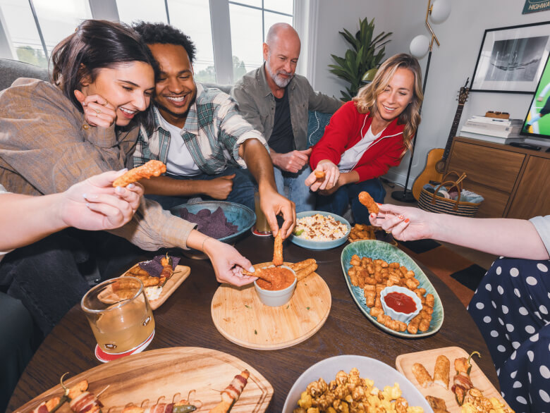 Group of people gathered around a table dipping mozzarella sticks and fried snacks into sauces