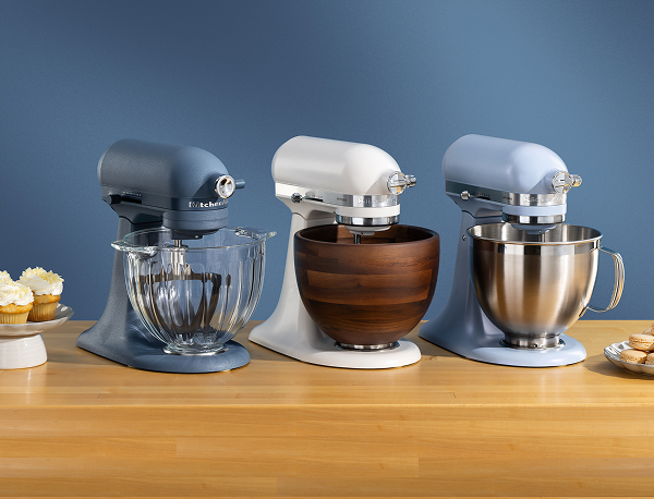 Blue, white and blue stand mixers on a wooden counter with different plates of pastries.