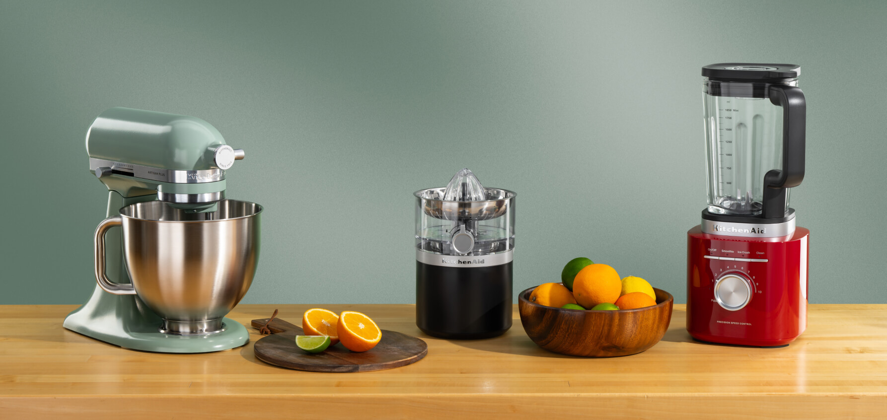 A teal stand mixer, black citrus juicer and red blender on a wooden counter with assorted citrus