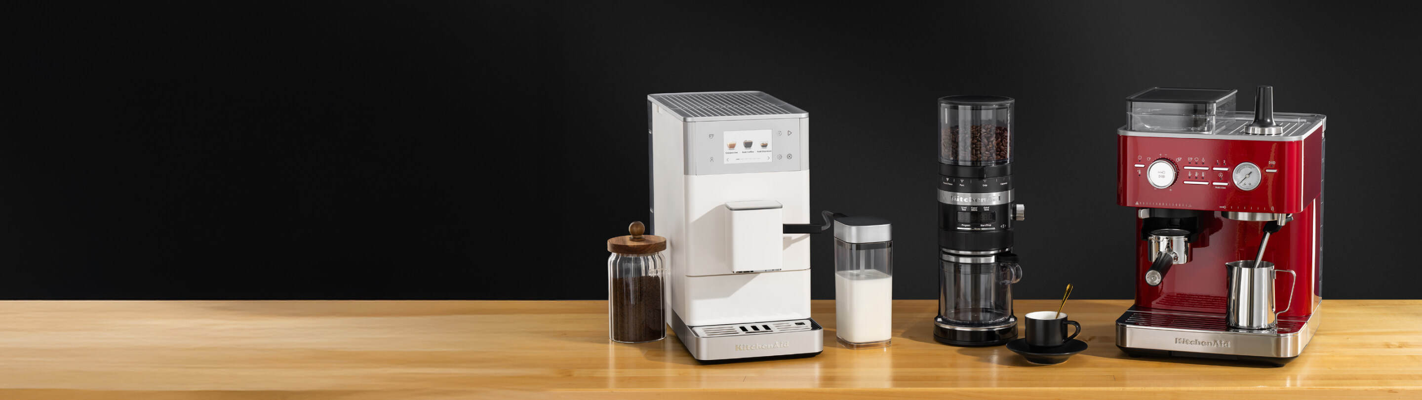 Various KitchenAid® coffee and espresso makers on a wooden counter surrounded by coffee ingredients