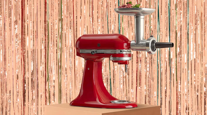 A KitchenAid® stand mixer with grinder attachment in front of a shiny decorative background
