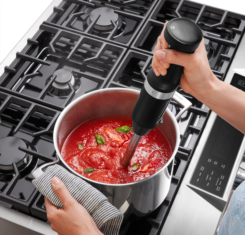 Black hand blender mixing tomato sauce.