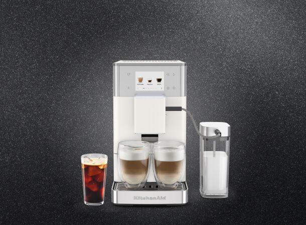 White KitchenAid® espresso machine with a touchscreen drink menu, beside an espresso martini and espresso against a dark background
