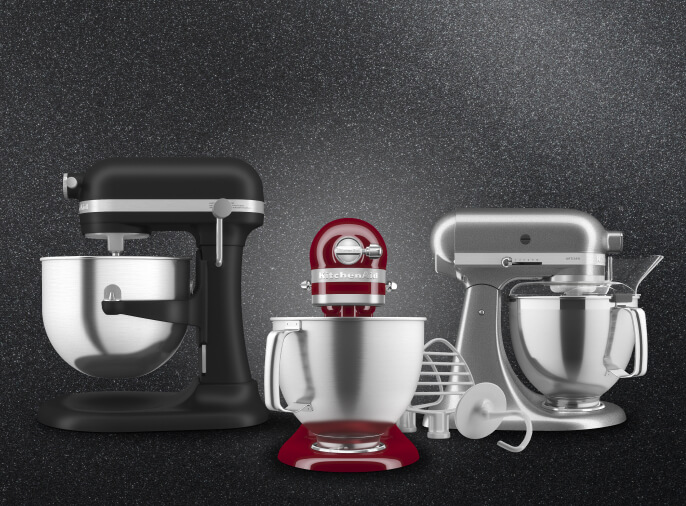 Three KitchenAid® stand mixers in black, red, and silver against a dark background, each fitted with different attachments
