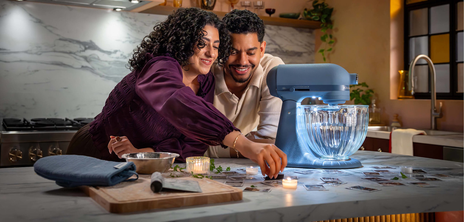 Couple looking at photos on a candlelit kitchen counter beside a KitchenAid® Design Series Luminaire Stand Mixer