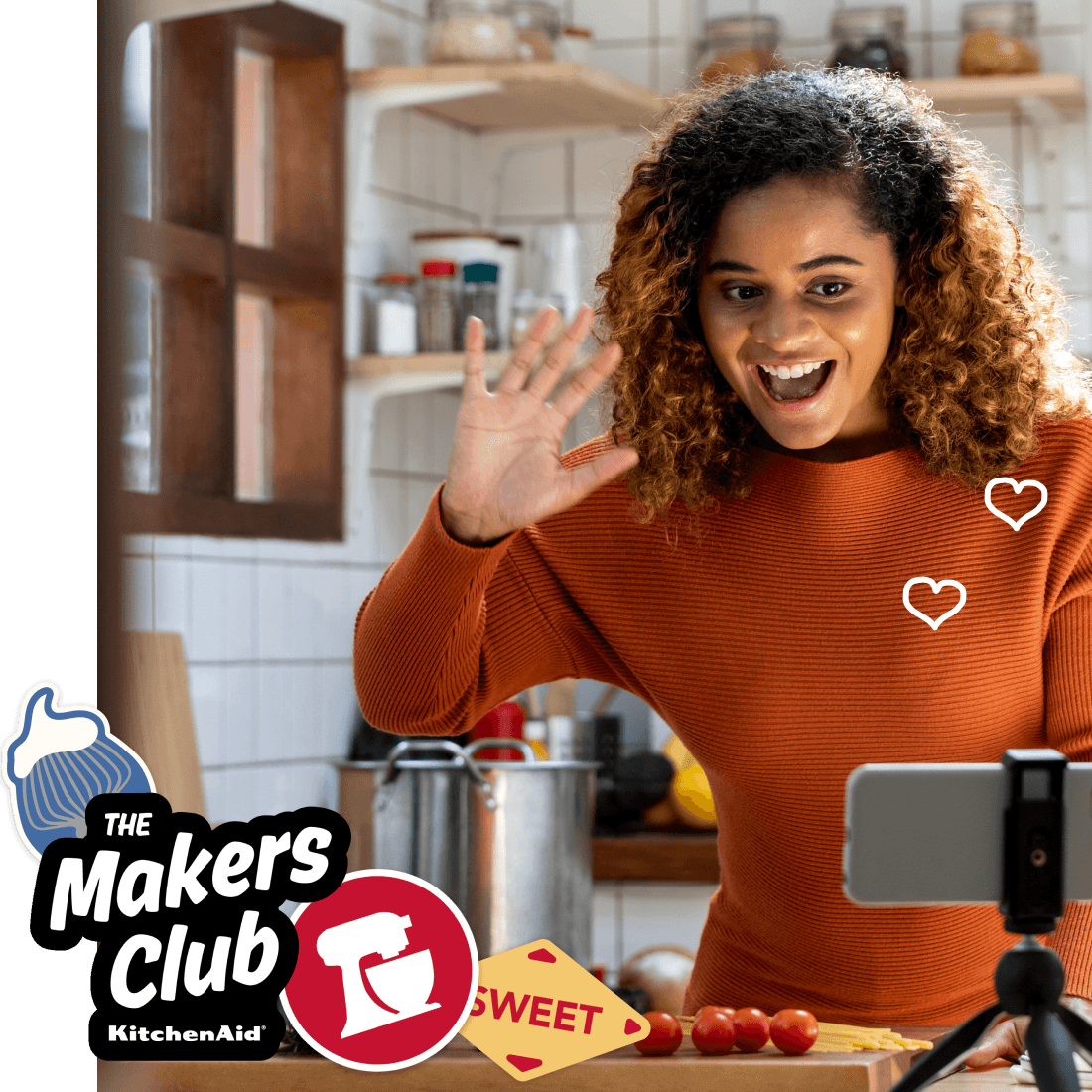 A person recording themselves in the kitchen with a KitchenAid Makers Club logo over it