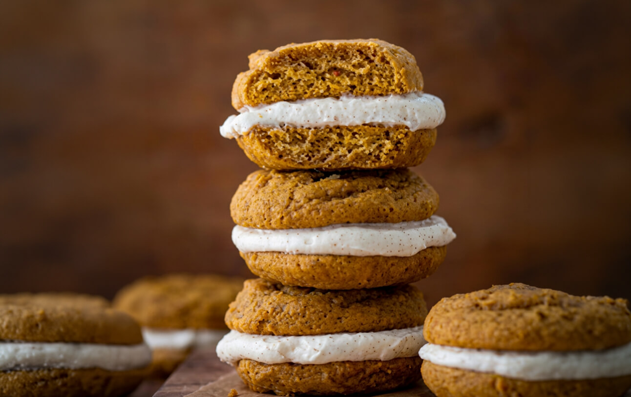 Stacked pumpkin sandwich cookies filled with cream frosting