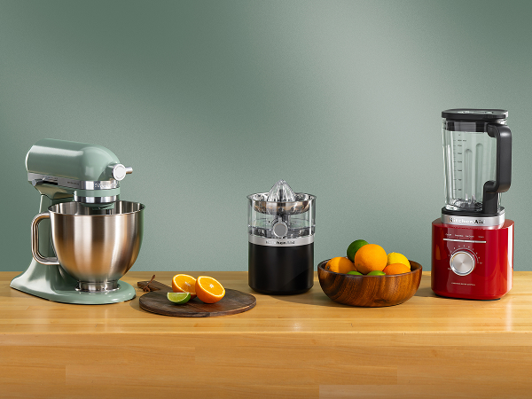 Green KitchenAid® stand mixer, black citrus juicer and red blender on a wooden counter with oranges