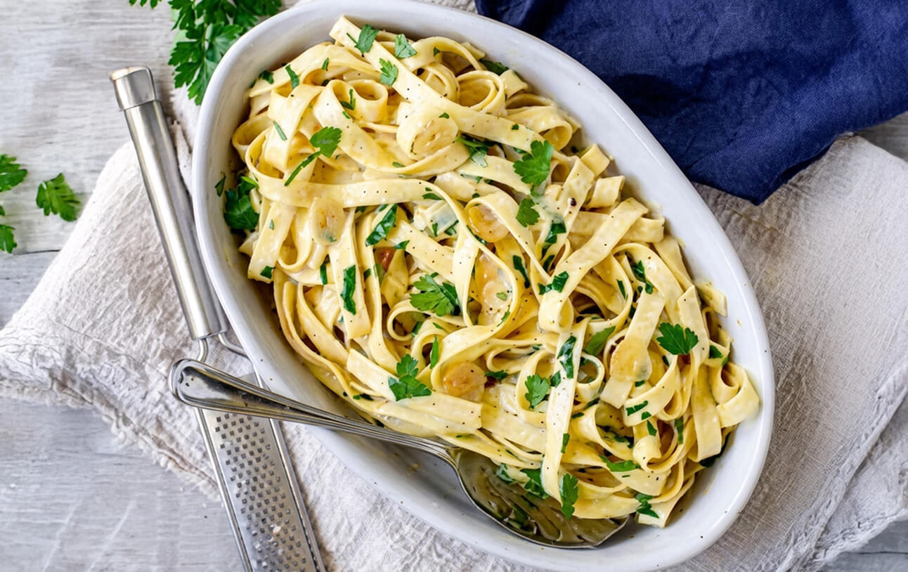 Fettuccine tossed in a creamy sauce and garnished with parsley in a white dish