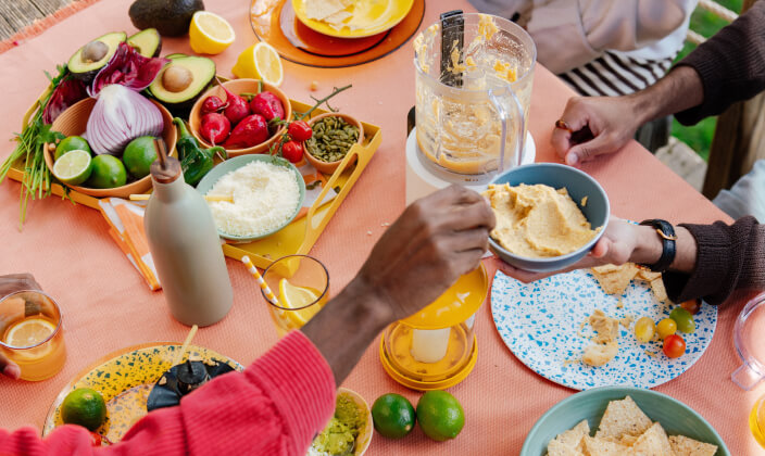 People enjoying vegetables and hummus with a KitchenAid® chopper in the center of a table