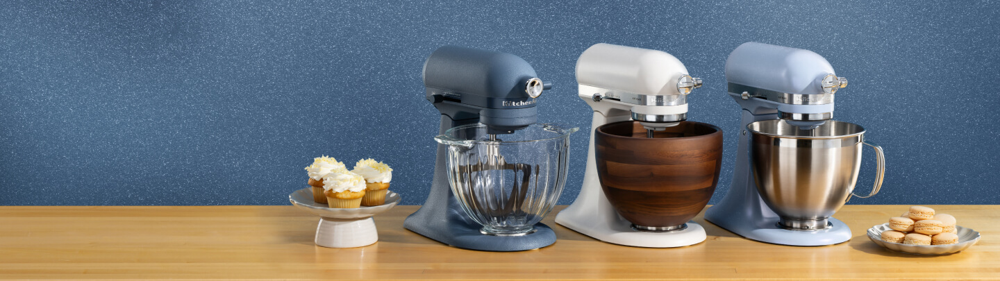 Blue, white and blue stand mixers on a wooden counter with different plates of pastries.