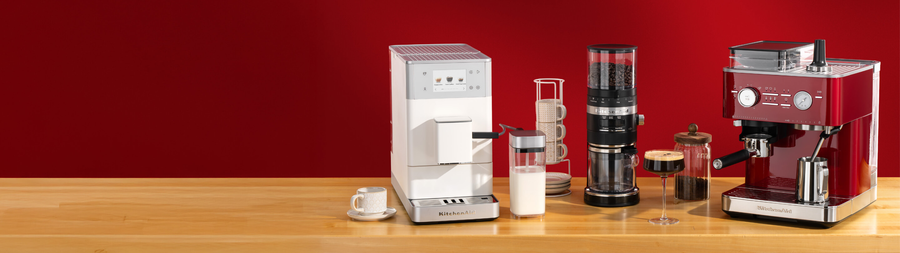 A white automatic espresso machine, black bean grinder and red espresso machine on a wooden countertop