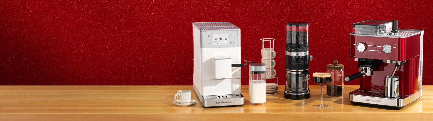 A white automatic espresso machine, black bean grinder and red espresso machine on a wooden countertop