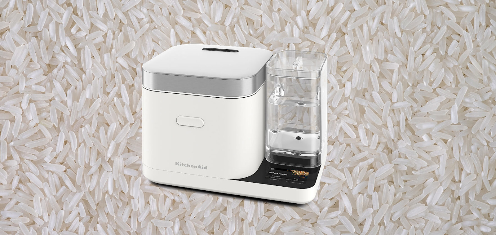 White KitchenAid® rice cooker set against a background of uncooked rice
