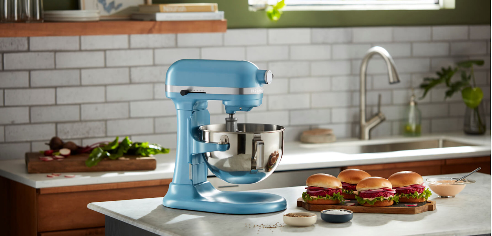 Blue KitchenAid® stand mixer on a counter beside a tray of burgers