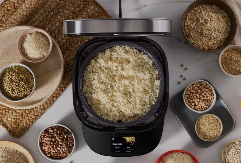 KitchenAid® grain and rice cooker filled with cooked rice, surrounded by bowls of assorted grains and beans