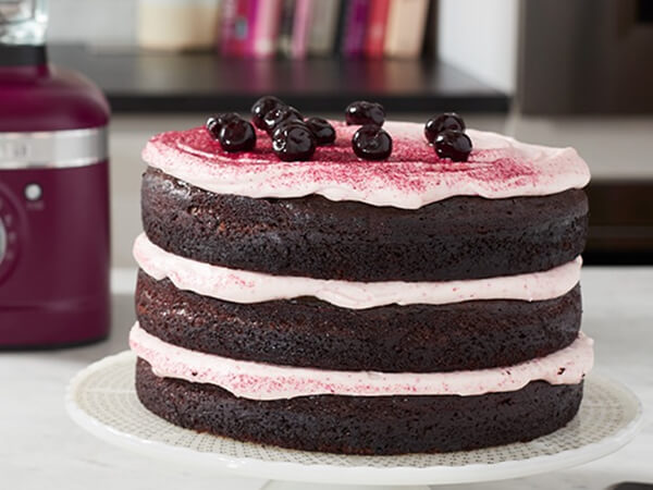 A layered chocolate cake topped with better powder and cherries