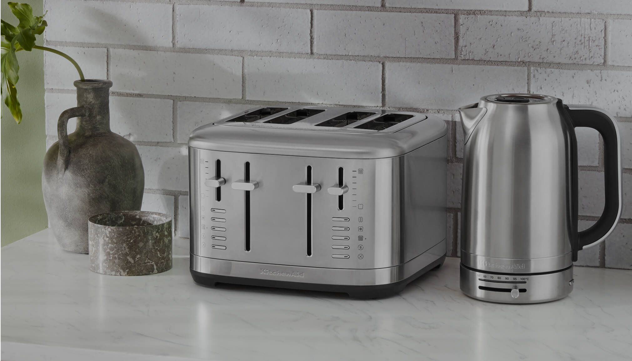 Stainless steel KitchenAid® four-slot toaster and electric kettle on a marble counter