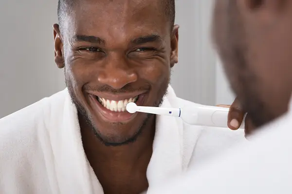 A man looks into a mirror and smiles as he brushes his teeth.