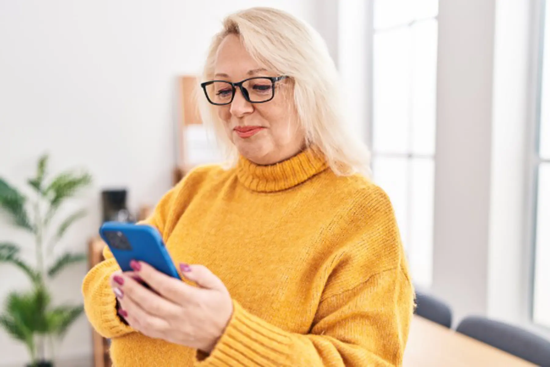 A senior woman in a yellow sweater looks down at her cellphone. 