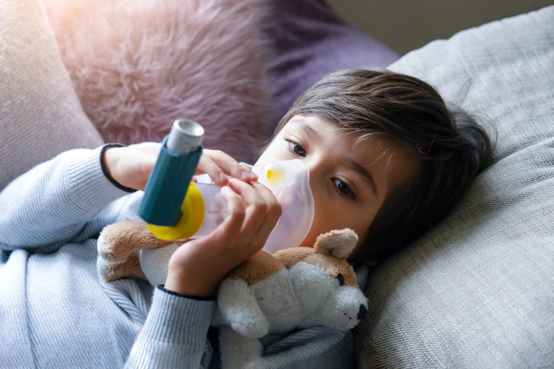 A child lies down and holds their inhaler chamber to their face.