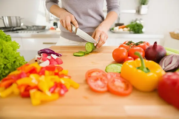 A woman stands at a counter and cuts vegetables.