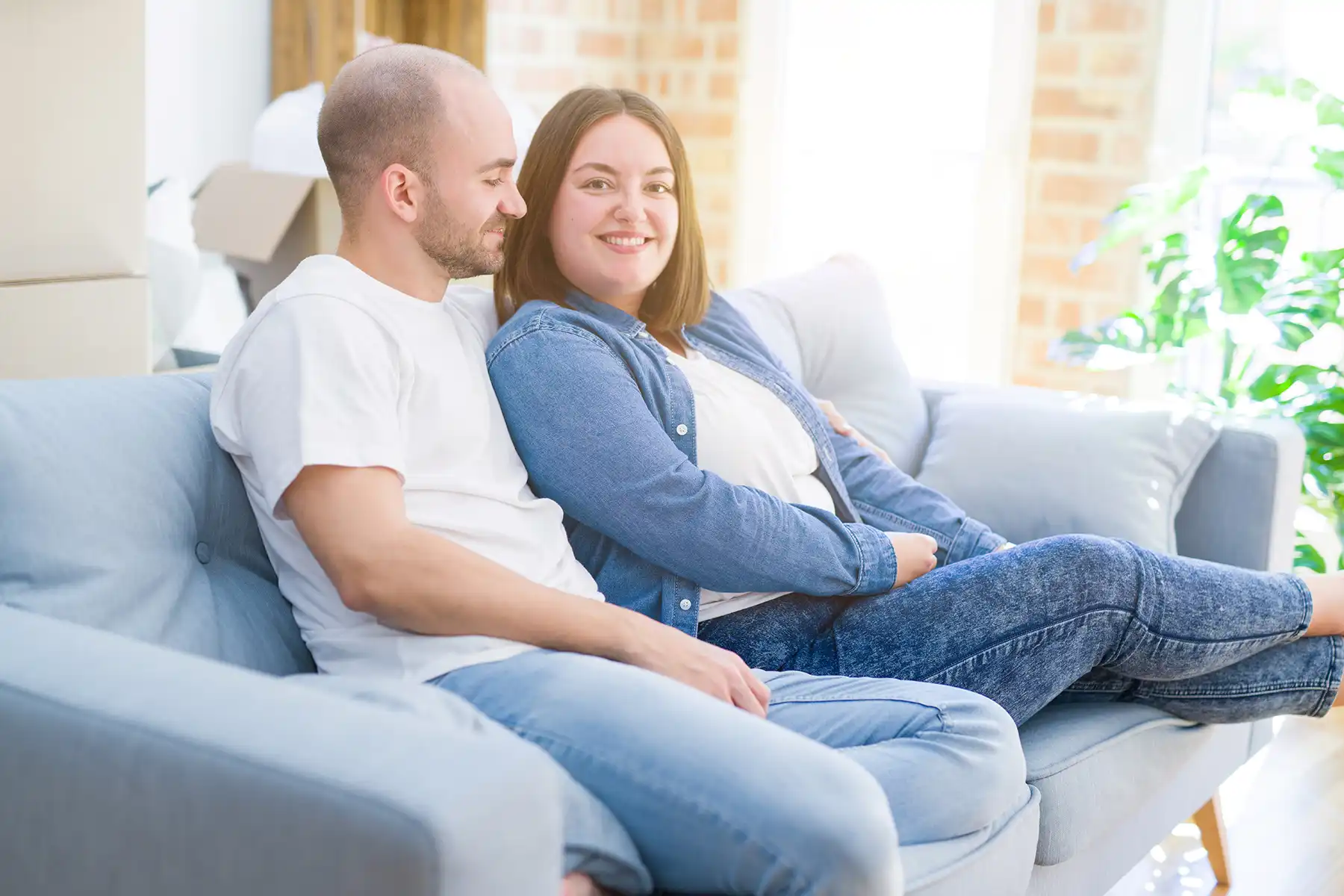 Man and woman sitting on couch, man looks at her while she looks into the camera.