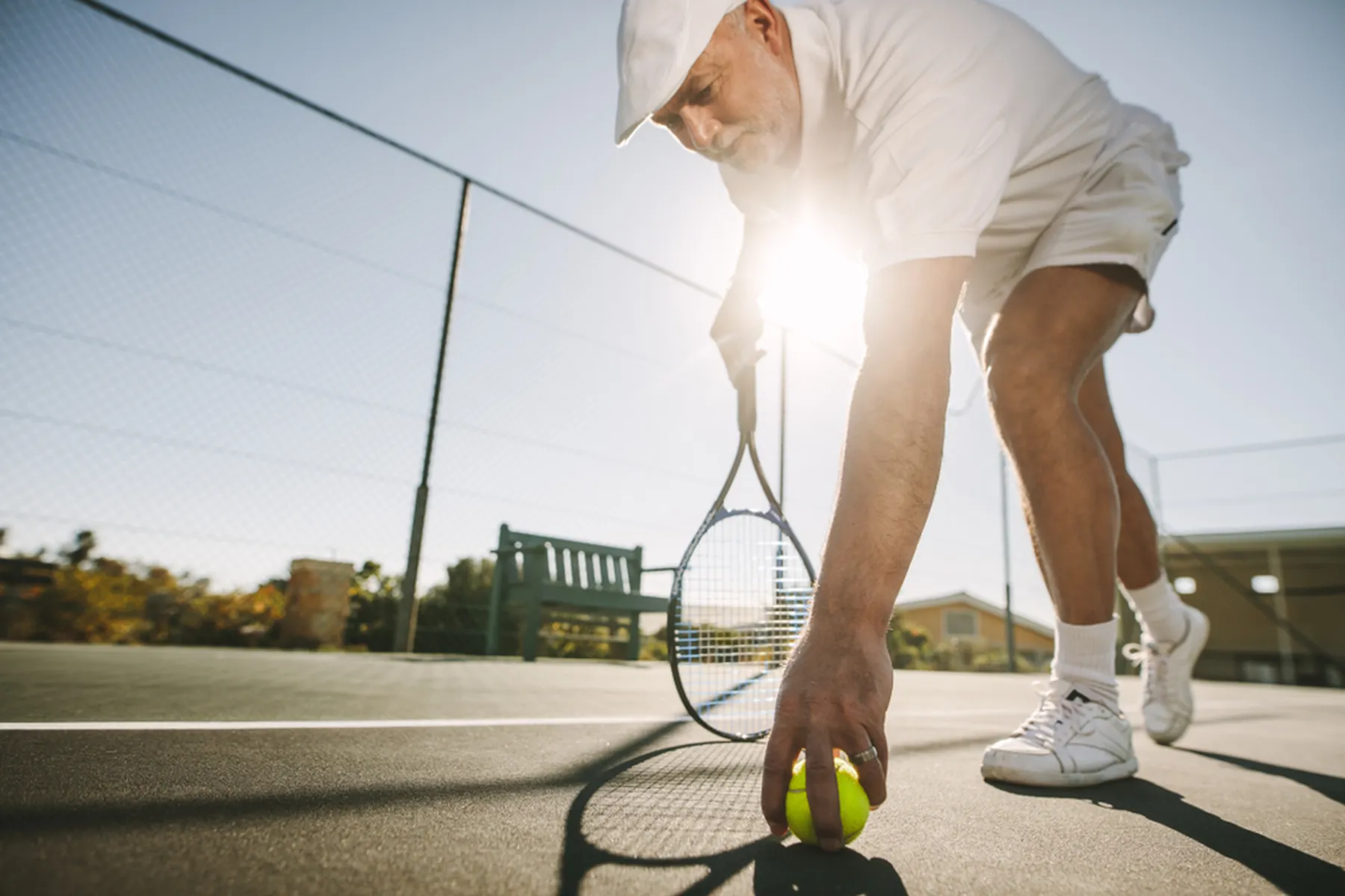 A man leans over to pick up a tennis ball.