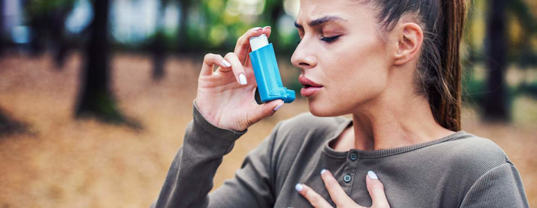 Eine junge Frau steht im Wald und benutzt Asthmaspray.