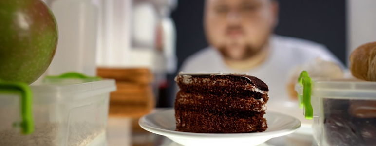 Es ist ein Mann zu sehen, der die Kühlschranktür öffnet. Im Fokus des Bildes ist ein Schokokuchen.