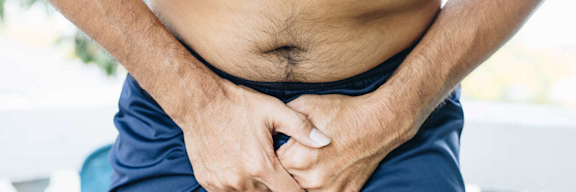 Mann hält sich vor Schmerzen den Schritt.