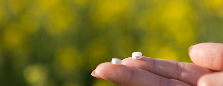 Zwei kleine weiße Tabletten werden auf den Fingerspitzen gehalten.