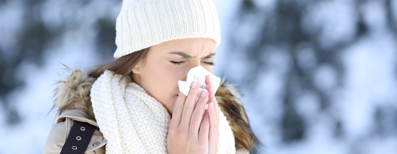 Eine Frau mit winterlicher Kleidung und Schnee im Hintergrund putzt sich die Nase.
