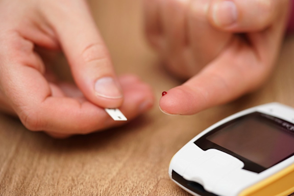 Blutzuckermessung bei Diabetes. Patient hat Bluttropfen am Finger. Teststreifen und Messgerät sind einsatzbereit.