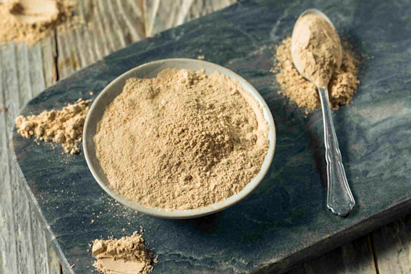Gelbes Maca-Pulver in einer Schüssel und auf einem Löffel.