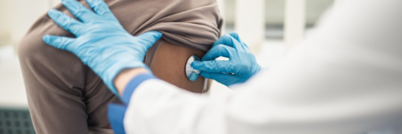 Ein Arzt hört mit dem Stethoskop am Rücken einer Patientin die Lunge ab.