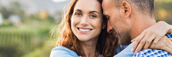 Glückliches Paar umarmt sich vor einer verschwommenen Bergkulisse.