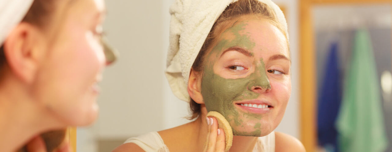 Junge Frau vor dem Spiegel im Badezimmer mit einer Gesichtsmaske aus Heilerde.