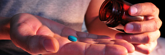 Aus einer Glasflasche schüttet ein Mann sich eine blaue Tablette auf die Handfläche.