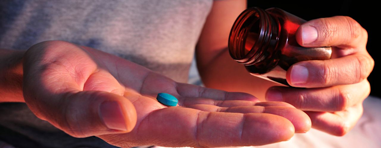 Aus einer Glasflasche schüttet ein Mann sich eine blaue Tablette auf die Handfläche.