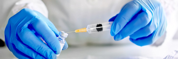 Hände mit blauen Handschuhen bereiten eine Spritze mit Impfstoff vor.