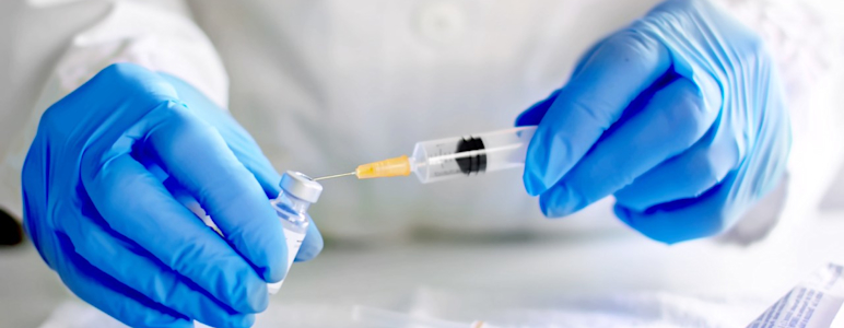 Hände mit blauen Handschuhen bereiten eine Spritze mit Impfstoff vor.